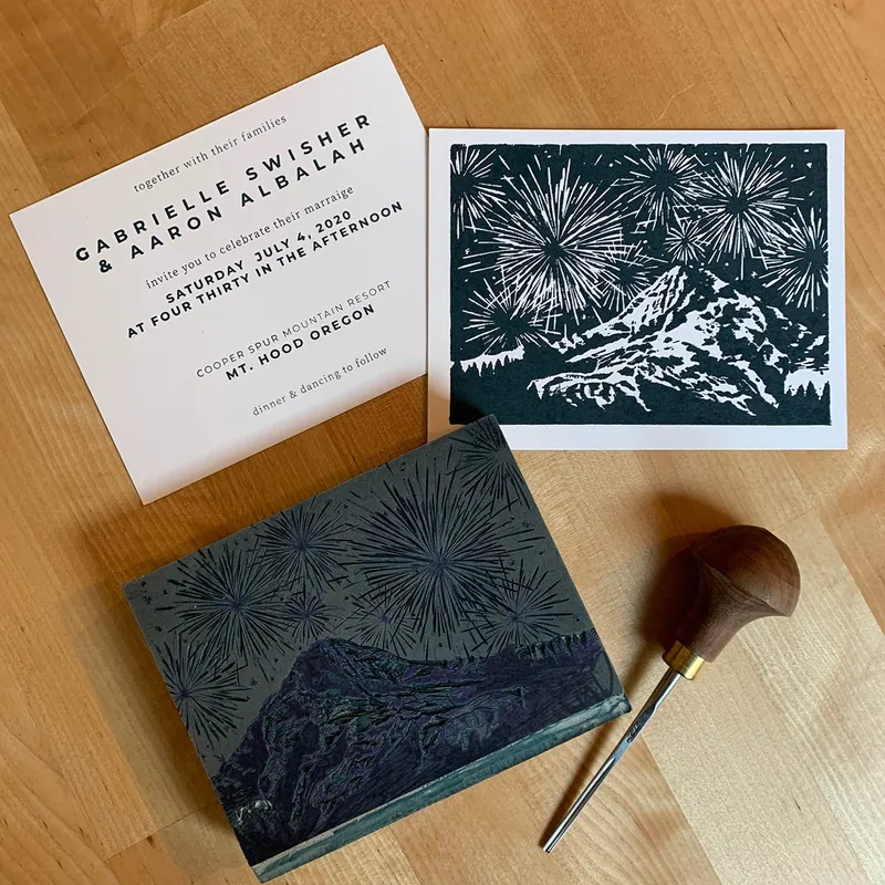 Letterpress wedding invitation next to a block print of fireworks over Mt. Hood and its carved block