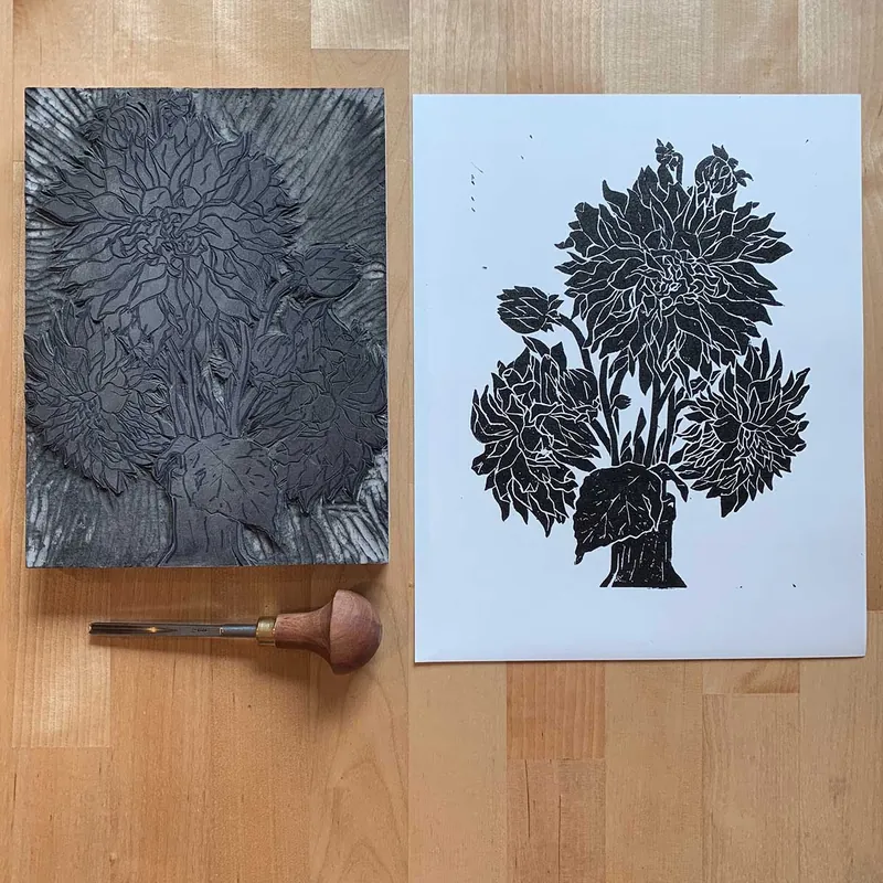 Carved linoleum block and printed sheet of a dahlia bouquet, with a carving tool